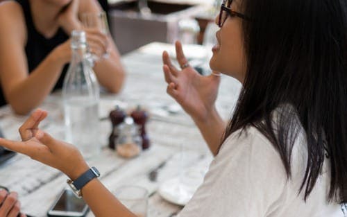 how-to-stop-interrupting-people-woman-at-table-gesturing-speaking